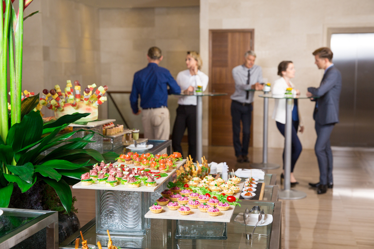 View of different canapes, tartlets and snacks on buffet table in restaurant. Business people eating and talking in background. Catering concept